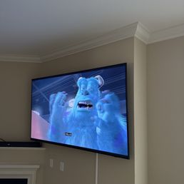 Perfect work! - A flat-screen TV mounted on a beige wall shows a scene from Monsters Inc featuring a blue monster with an expressive face.