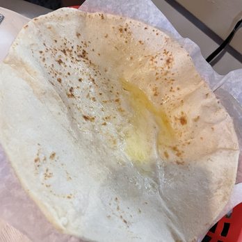 Duran Central Pharmacy - Tortilla with butter. Bomb!!! - A partially eaten, thin, crispy tortilla with melted butter on top is shown. The tortilla appears lightly browned and is placed on parchment paper, likely served at a restaurant or food establishment. The background includes a table surface and part of a red basket, indicating a dining environment. - Mexican Near Me - Albuquerque, New Mexico