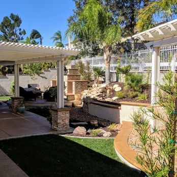 Royal Design Builders - Aluminum Patio Cover with Stone Columns also a Outdoor Fireplace on raised deck and a Trellis with a Hammock Turf and Water Feature - Patio Coverings Near Me