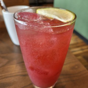 First Watch - A tall glass filled with a pink, icy drink garnished with lemon slices, placed on a wooden table in a restaurant setting. - Breakfast & Brunch Near Me - Stuart, Florida