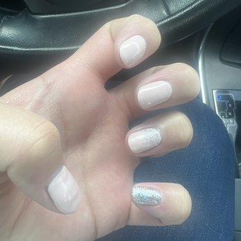 Flashy Nails - A person's hand with manicured nails, featuring a mix of plain and glittery designs, is resting on a car's steering wheel. - Nail Salons Near Me - Albuquerque, New Mexico