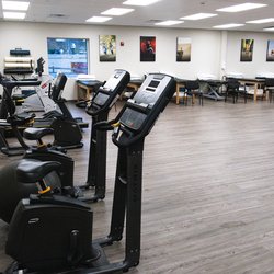MOTION Sports Medicine - Nyack - Wide-angle view of MOTION Nyack's therapy room with several Matrix exercise bikes and SCI-FIT machines, treatment tables in a sleek clinic