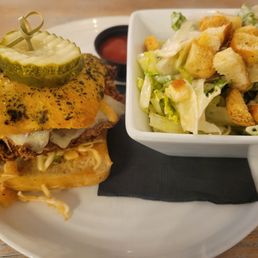Kama Jama Chicken Sandwich - A chicken sandwich with pickles on a bun, accompanied by a side salad of lettuce and croutons in a white bowl.