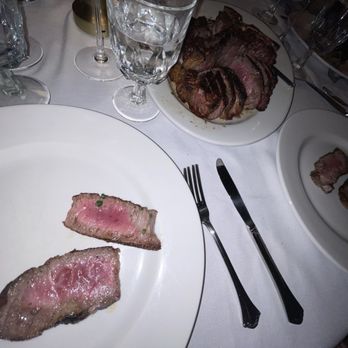 Pace's Steakhouse - Porterhouse Steak - Raw and cooked steak slices are displayed on white plates, with wine glasses and utensils on a dining table, indicating a steakhouse setting. - Steakhouses Near Me - Hauppauge, New York