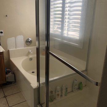 EDW Construction - Before - Bathroom featuring a bathtub with a shower stall, a window with blinds, and toiletries on the floor and ledge. - General Contractors Near Me
