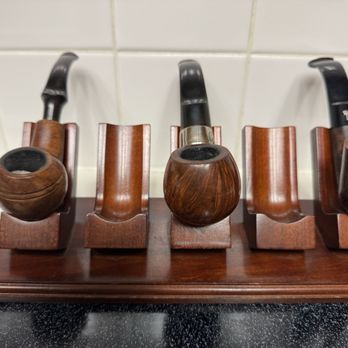 Iwan Ries - Five wooden smoking pipes are arranged on a wooden stand against a tiled wall, showcasing different shapes and finishes. - Tobacco Shops Near Me - Chicago, Illinois
