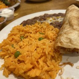 Rice, beans, chicken flauta - A plate featuring Mexican cuisine includes seasoned rice, refried beans, and a chicken flauta, served on a white dish.