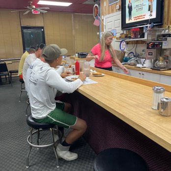 Old Dixie Cafe - Counter seating and Lisa - A woman in a pink shirt serves food at a counter in a cafe with three customers seated and eating. - Diners Near Me - Jupiter, Florida