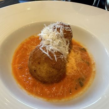 Il Piatto - Arancini - Two arancini balls topped with shredded cheese are served on a tomato-based sauce in a white bowl, at an Italian restaurant. - Italian Near Me - Washington, DC, District of Columbia