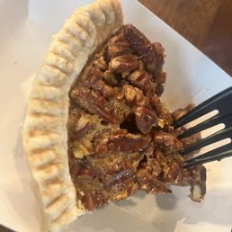 Slice Pecan Pie - A slice of pecan pie with a golden, flaky crust and a filling of chopped pecans, served in a white paper tray.