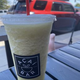Pineapple Mint - A pineapple mint smoothie in a clear plastic cup with a red straw, placed on an outdoor table at a café.