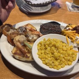 Steak and shrimp combo with sides of loaded potatoe and corn