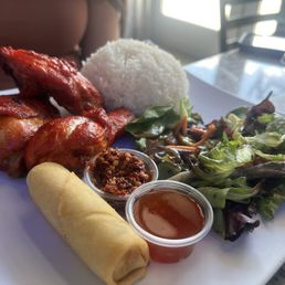 A plate featuring grilled chicken, a rice ball, mixed salad, spring roll, and two dipping sauces, served at Rice Box & Boba in Albuquerque.