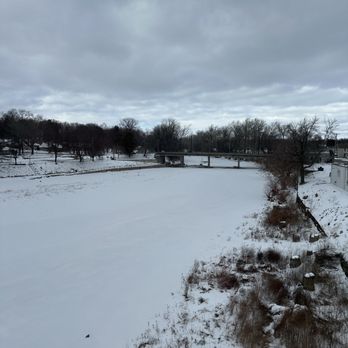 Firewater Mill - Winter river view - A snow-covered river with a bridge in the background, surrounded by leafless trees and overcast sky. - American Near Me - Marion, Indiana