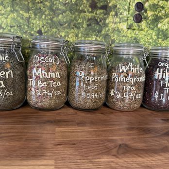 Chipko Market - Loose leaf teas - Six glass jars containing various loose leaf teas, labeled with names and prices, are displayed on a wooden surface in front of a nature-themed background. - Specialty Food Near Me - St. Charles, Illinois
