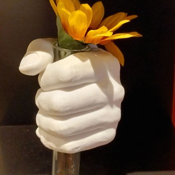 The Phillips Collection - A sculpture depicts a white hand with detailed fingers gripping a small glass vase. The vase contains yellow flowers with multiple petals. The background is dark, highlighting the sculpture and flowers. The sculpture appears to be made of a smooth material, and the flowers are artificial or decorative. - Art Museums Near Me - Washington, DC, District of Columbia
