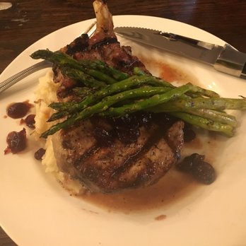 Mugsy's Grubhouse - 16oz double bone in pork chop topped with apple cranberry compote and served with grilled asparagus on a bed of garlic mashed potatoes. - Steakhouses Near Me - Yale, Oklahoma