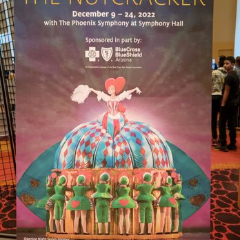 Symphony Hall - The poster features a colorful illustration of a Nutcracker-themed scene with a ballerina atop a large, decorated nutcracker castle, surrounded by dancers dressed as elves or toy soldiers. It provides details about the performance dates, location at Symphony Hall, and sponsorship by BlueCross BlueShield Arizona. The background has a gradient sky with clouds, and the overall design is vibrant and theatrical. - Performing Arts Near Me - Phoenix, Arizona