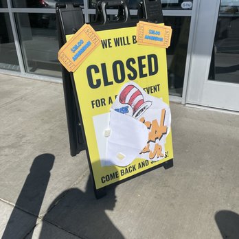 Electric Playhouse - Closed sign - A portable signboard with a yellow background and black text states the business is closed, with tickets and a paper attached, outside a glass storefront. - Party & Event Planning Near Me - Albuquerque, New Mexico