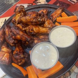 Double Down Wings - Buffalo chicken wings with two dipping sauces and carrot sticks are served on a black plate at a restaurant table, with photos and a red table surface in the background.
