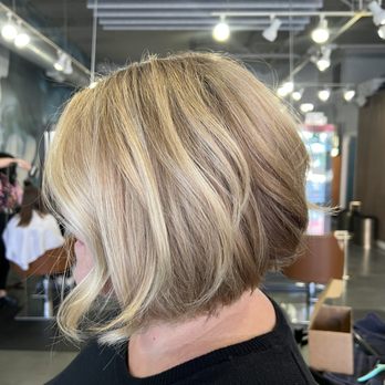 Epoch Studio Salon - Chicago - A woman with a short, layered blonde hairstyle is seated in a salon. The haircut features a side part with soft, textured layers. The salon interior includes ceiling lights, a dark wall, and other clients or staff in the background. The image is focused on the hairstyle, with the salon environment visible behind her. - Hair Extensions Near Me - Chicago, Illinois