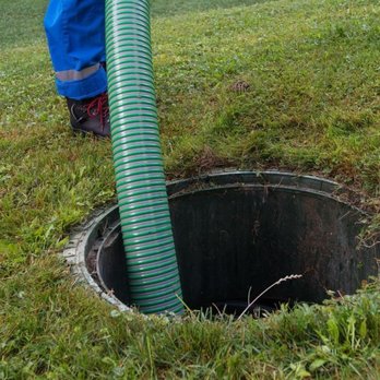Superior Septic And Clean Can - A service technician in blue work trousers and boots stands on a green lawn, guiding a large, ribbed green suction hose into ... - Septic Services Near Me - Round Rock, Texas Superior Septic And Clean Can - A service technician in blue work trousers and boots stands on a green lawn, guiding a large, ribbed green suction hose into ... - Septic Services Near Me - Round Rock, Texas