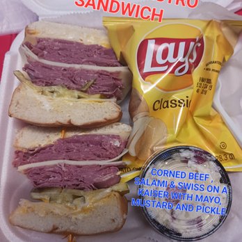 Simon's Pub - a bag of chips and a sandwich - A sandwich featuring corned beef, salami, Swiss cheese, and a Kaiser roll, accompanied by Lay's classic chips and a side salad with mustard and pickle. - Dive Bars Near Me - Dunedin, Florida
