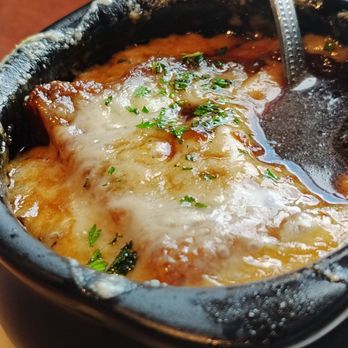Ford's Garage Florence - Great onion soup - A close-up of French onion soup served in a black bowl, topped with melted cheese and garnished with chopped herbs. - Burgers Near Me - Florence, Kentucky