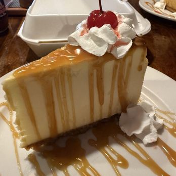 Bubb's Grub - Cheese cake with extra caramel - A slice of cheesecake with caramel drizzle, topped with whipped cream, a cherry, and a maraschino cherry stem, served on a white plate. - Barbeque Near Me - Catalina, Arizona
