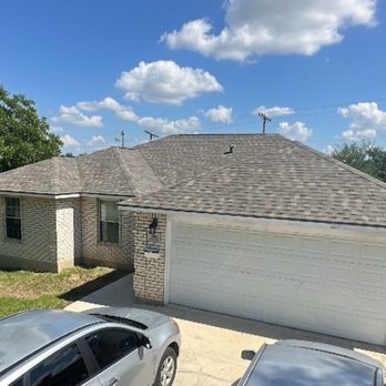 NEMA Roofing Solutions - Our new roof - A brick house with a gabled roof, a white garage door, and a concrete driveway, set in a suburban neighborhood. - Roofing Near Me - Oxnard, California