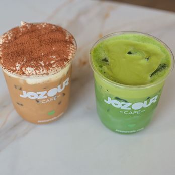 Jozour Cafe - Two iced beverages in clear cups with 'Jozour' branding, one with a brown, frothy top and cocoa powder, the other with a green, swirled appearance, placed on a white surface. - Coffee & Tea Near Me - Braintree, Massachusetts