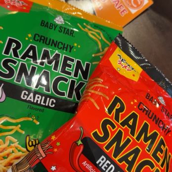 Eggroll Cafe - Ramen chips!!!! Garlic is the best of the two - The image features two bags of ramen snack chips, one green garlic-flavored and one red chili-flavored, placed in front of an orange Eggroll Cafe menu booklet. The snack bags display colorful graphics and branding, with the garlic flavor emphasizing a savory profile and the red chili flavor indicating spiciness. The Eggroll Cafe menu booklet in the background suggests a fusion Asian cuisine setting, highlighting snack options alongside a broader menu of dishes. - Coffee & Tea Near Me - Lowell, Massachusetts
