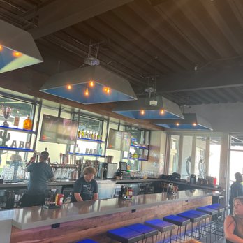 Topgolf - Mildly busy and staff has yet to come up to take an order. - A bar with a long counter and stools, bartenders working behind the bar, and multiple TV screens mounted on the wall, with patrons seated nearby. - New American Near Me - Albuquerque, New Mexico