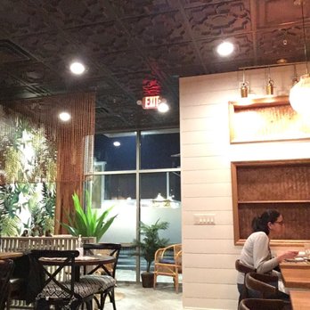 Imm Thai - Interior view - The image shows the interior of a restaurant with various seating options, plants, and decorative elements, including a woman sitting at the bar. - Thai Near Me - Clark, New Jersey