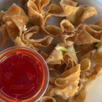 Dragon Restaurant - Cheese fried wontons - A serving of fried wontons with crispy, golden-brown wrappers, accompanied by a small container of red dipping sauce, likely sweet and sour or chili. - Chinese Near Me - Ogden, Utah