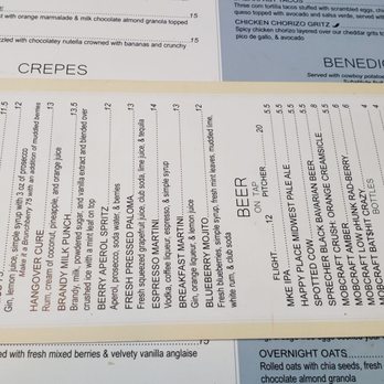 Brunch Berry - 07/24 - A menu from The Bar displays a list of house cocktails and beers, including options like Mimosa, Blood Mary, Hangover Cure, Berry Apple Spritz, and Blueberry Martini. The menu is printed on a white background with black text, and it is placed on top of other menu pages that feature food items such as crepes, Benedicts, and oatmeal. The menus are arranged on a dark wooden surface. - Coffee & Tea Near Me - New Berlin, Wisconsin