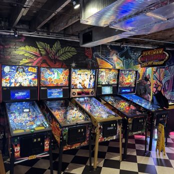 Secret Level - Multiple pinball machines with themed artwork, including Star Wars and WrestleMania, are lined up in an arcade with graffiti-style wall art. - Arcades Near Me - Arvada, Colorado