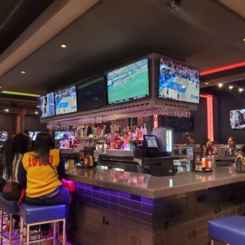 Topgolf - a group of people sitting at a bar watching televisions - New American Near Me - Edison, New Jersey Topgolf - a group of people sitting at a bar watching televisions - New American Near Me - Edison, New Jersey