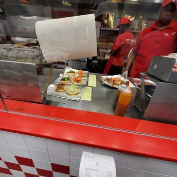 Five Guys - a man in a red shirt standing in front of a counter with food on it - Burgers Near Me - Brooklyn, New York Five Guys - a man in a red shirt standing in front of a counter with food on it - Burgers Near Me - Brooklyn, New York