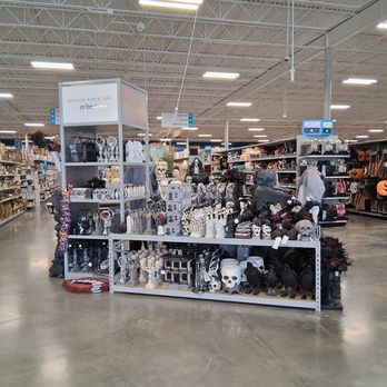 At Home - A store aisle features a display of Halloween decorations, including skulls, black cats, and spooky ornaments, with shelves of other home decor items in the background. - Home Decor Near Me - Euless, Texas