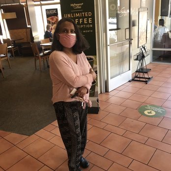 Panera Bread - A woman with shoulder-length dark hair, wearing a pink face mask and pink sweater, stands inside a Panera Bread in Leesburg, VA. - Sandwiches Near Me - Leesburg, Virginia