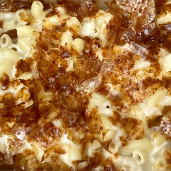 Seed Shack - Truffle Bacon Mac & Cheese-Truffle cashew cream & rice made bacon bites, 7.16.2022. - The image shows a close-up of a baked macaroni and cheese dish with a creamy cheese sauce and a crispy, golden-brown topping, likely bacon bits or breadcrumbs. The pasta is coated in cheese, and the topping adds texture and color contrast. - Vegan Near Me - Gilbert, Arizona