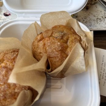First Watch - Orange Cranberry muffins!! Sooooo delicious - Two orange cranberry muffins are placed in a white takeout container, each lined with parchment paper, on a marble countertop. - Breakfast & Brunch Near Me - Gilbert, Arizona