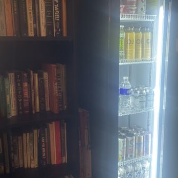 Classic Cups - A bookshelf with numerous books is positioned beside a glass-door refrigerator containing drinks like water, juice, and soda. - Coffee & Tea Near Me - Brooklyn, New York