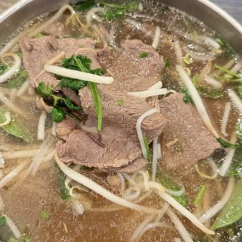 Pho Minh - #102. Pho Filet Mignon Soup - A bowl of Vietnamese pho containing beef slices, bean sprouts, herbs, and broth, with side dishes and utensils visible. - Soup Near Me - Temecula, California