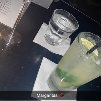 Blue Light - Drinks - The photo depicts a dark-colored table with a reserved sign, a glass of water placed on a napkin, and a margarita cocktail garnished with lime and lemon slices, with a straw. The setting appears to be in a bar or restaurant environment. - Bars Near Me - Chicago, Illinois