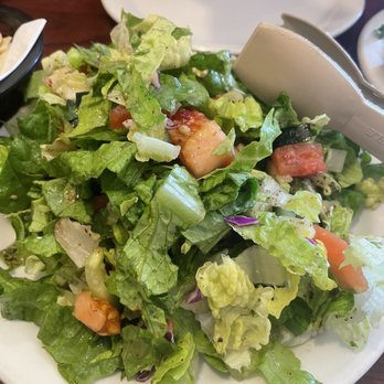 Oasis - A mixed green salad with lettuce, tomatoes, cucumbers, and purple cabbage on a white plate, with salad tongs nearby. - Mediterranean Near Me - Lexington, Kentucky