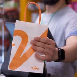 Vibe Cannabis - Close-up of a hand holding a Vibe by California branded shopping bag near a checkout scanner inside the cannabis dispensary.