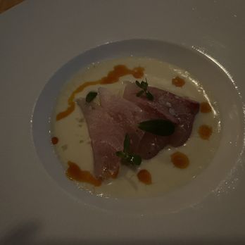 Ariete - Crudo - A dish with slices of raw fish, garnished with herbs and served with a sauce on a white plate. - New American Near Me - Miami, Florida