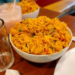 Shrimp Fried Rice - A large bowl of shrimp fried rice with vegetables such as peas and carrots, served on a wooden table in a restaurant setting.